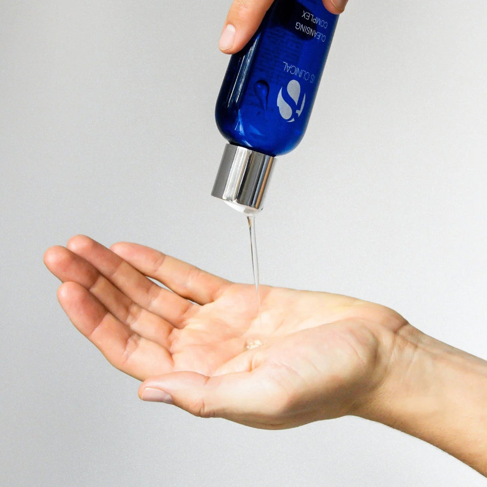 Blue bottle of skincare product being poured into a hand against a gray background