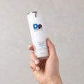 Hand holding a skincare serum bottle labeled 'DP Dermaceuticals' against a plain background