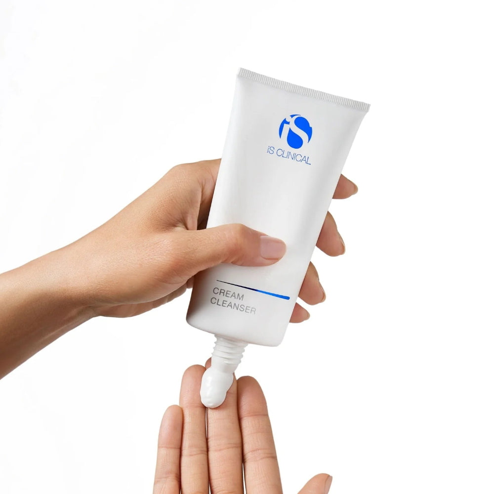 Hand holding a tube of cream cleanser with 'iS Clinical' branding on a white background