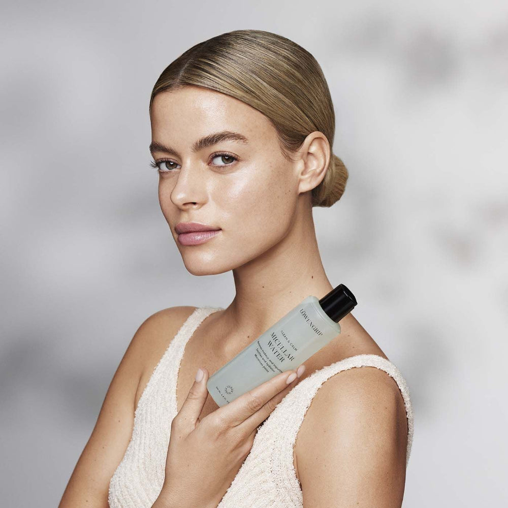 Woman holding a skincare product against a neutral background