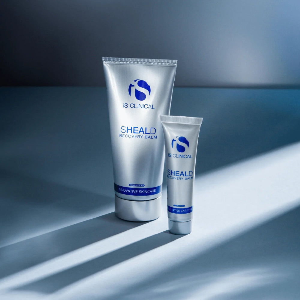 Two tubes of IS Clinical SHEALD Recovery Balm on a reflective surface with a gradient background